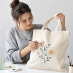 Une femme qui personnalise au pinceau son tote bag vierge